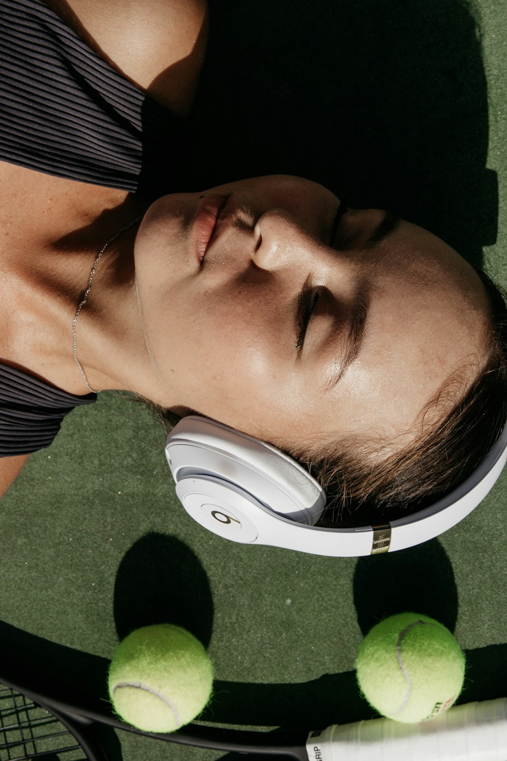 woman using white Beats headphones beside two green tennis ball