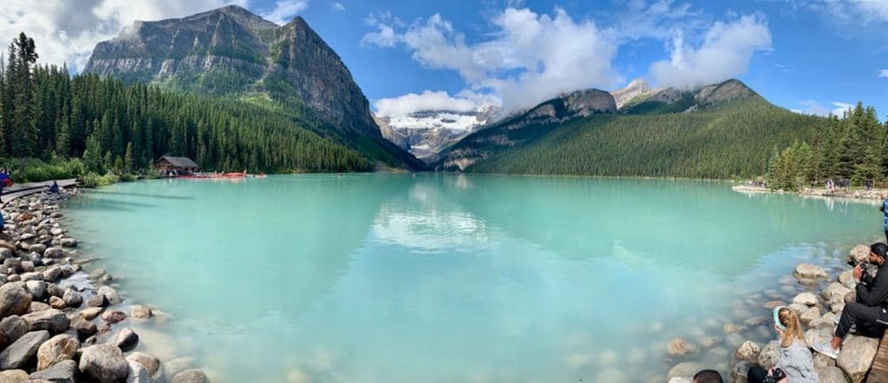 a group of people standing around a lake with mountains in the background