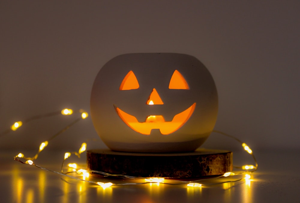 white and orange Jack-O-Lantern near yellow string lights