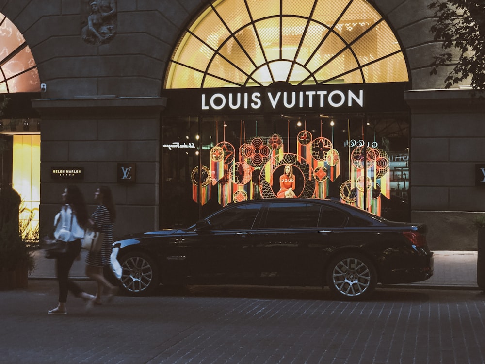 black sedan parking near Louis Vuitton building and two women walking near road