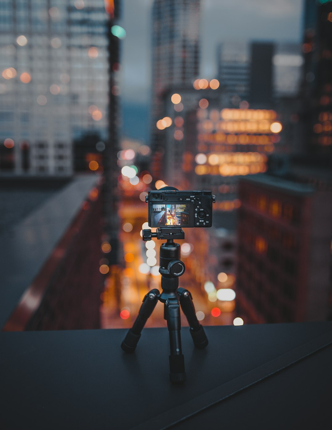 camera on tripod on building roof ledge at the city during night