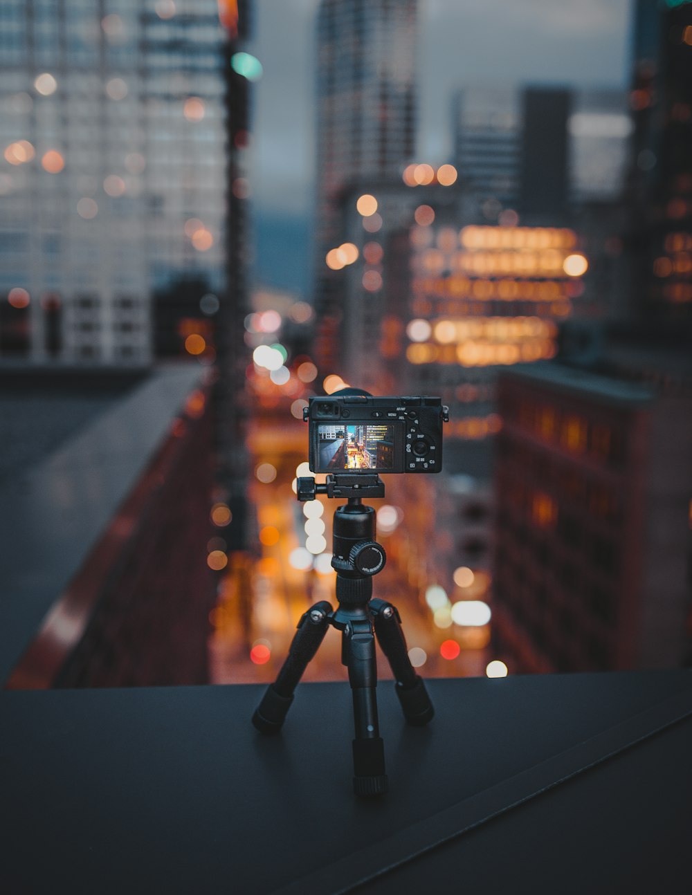 camera on tripod on building roof ledge at the city during night