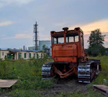 A rusted Caterpillar bulldozer parked in an industrial scrapyard under a cloudy sky.