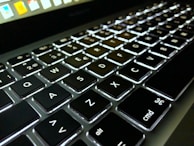Close-up of a premium laptop keyboard with backlit keys glowing in a dim room.