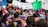 A large group of people engaged in a protest or rally. Many hold signs with various messages, including environmental and anti-capitalism statements. The crowd is diverse, with individuals wearing colorful clothing and face paint, conveying a sense of unity and activism. The atmosphere is lively and bustling.