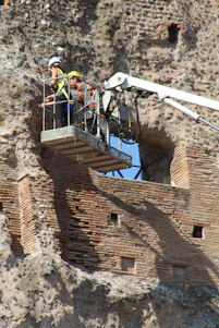 Skilled workers carefully restoring the brick façade of a historic building on a sunny day.