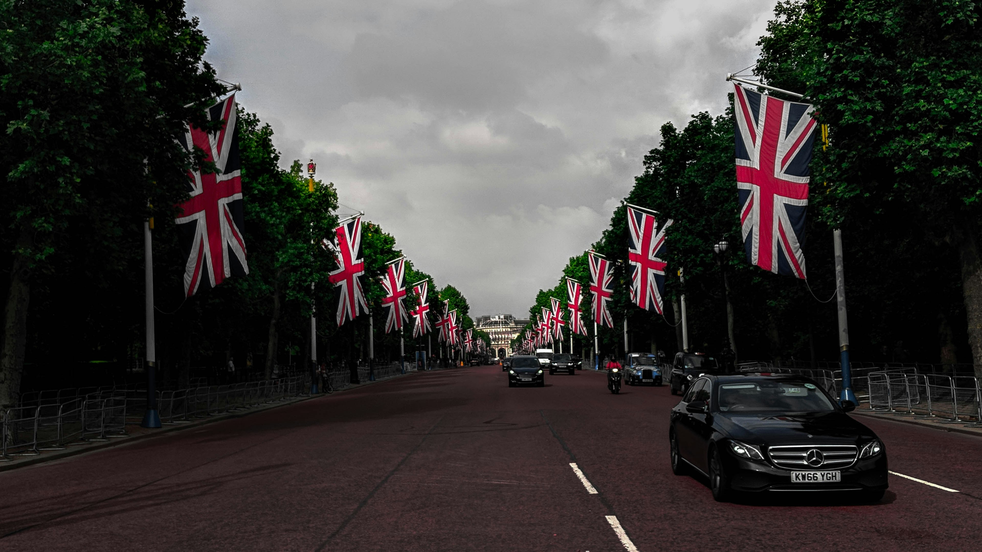 different vehicles on road showing United Kingdom flags surrounded with tall and green trees during daytime