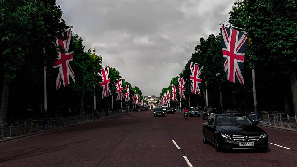 different vehicles on road showing United Kingdom flags surrounded with tall and green trees during daytime