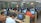 A large computer lab filled with many people seated at individual workstations. Each person is focused on the screen in front of them, with partitions separating each desk. The room is well-lit with fluorescent lights, and there are glass partitions creating smaller sections within the lab. The overall atmosphere suggests a busy, studious environment.