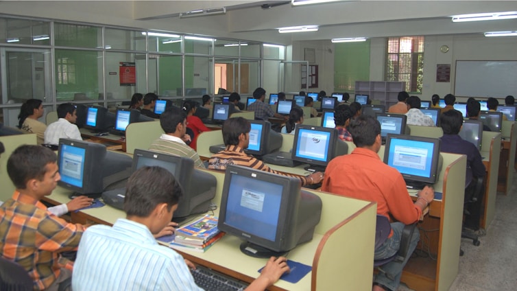 A bright, modern computer lab filled with rows of computers and focused staff assisting candidates during an online exam.