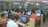 A large computer lab filled with many people seated at individual workstations. Each person is focused on the screen in front of them, with partitions separating each desk. The room is well-lit with fluorescent lights, and there are glass partitions creating smaller sections within the lab. The overall atmosphere suggests a busy, studious environment.