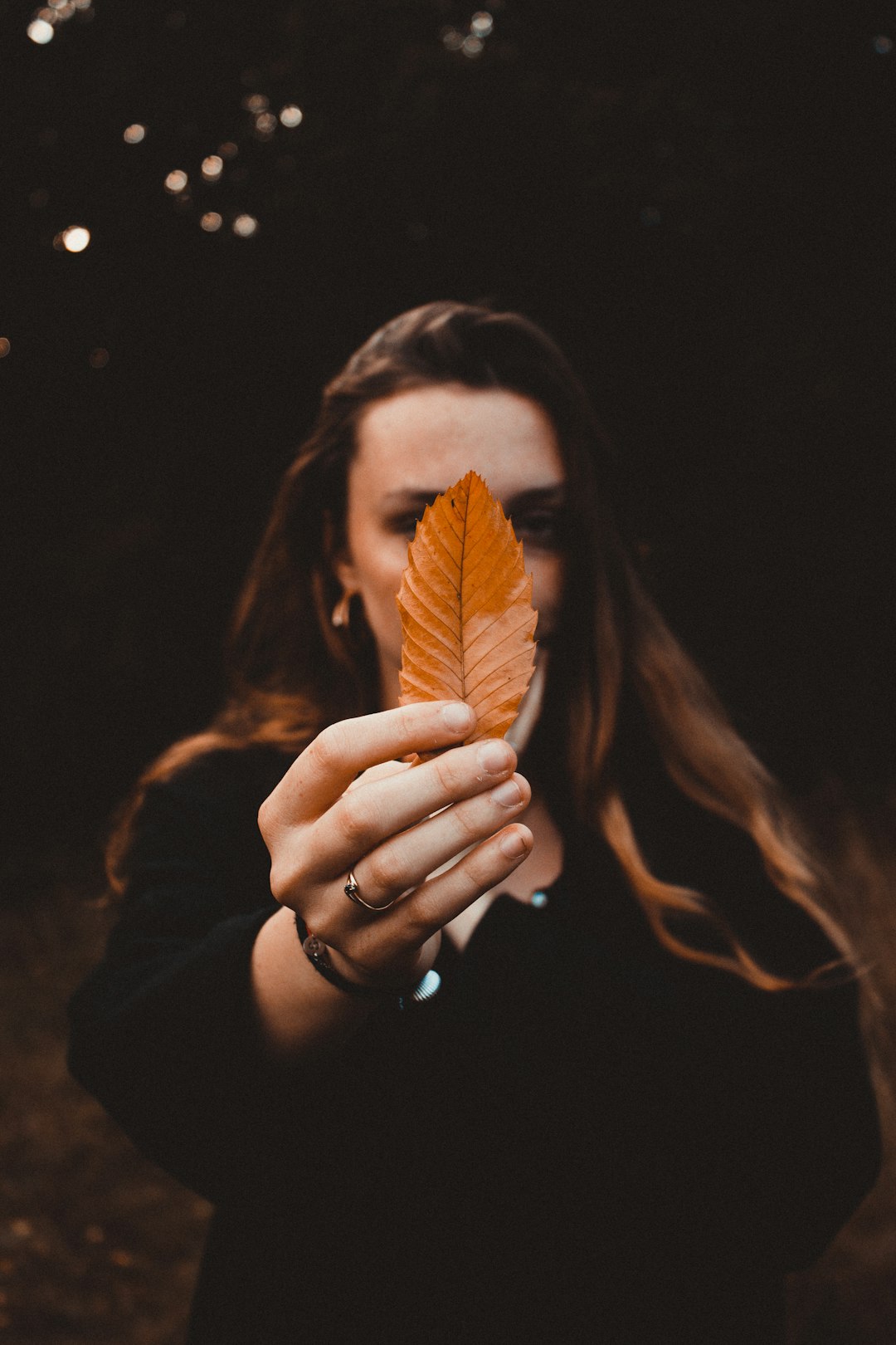 woman wearing black jacket holding brown ovate leaf while standing