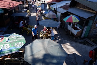 A vibrant street scene showing a candid moment of a street vendor interacting with a customer under colorful market umbrellas.