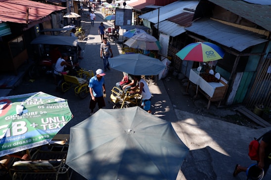 A vibrant street scene showing a candid moment of a street vendor interacting with a customer under colorful market umbrellas.