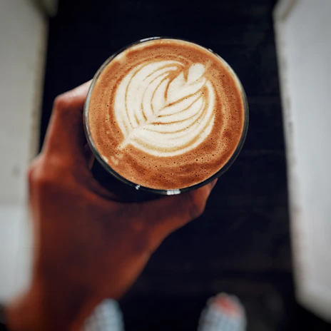 A hand holding a creamy latte with delicate leaf art against the backdrop of the mobile coffee shop.