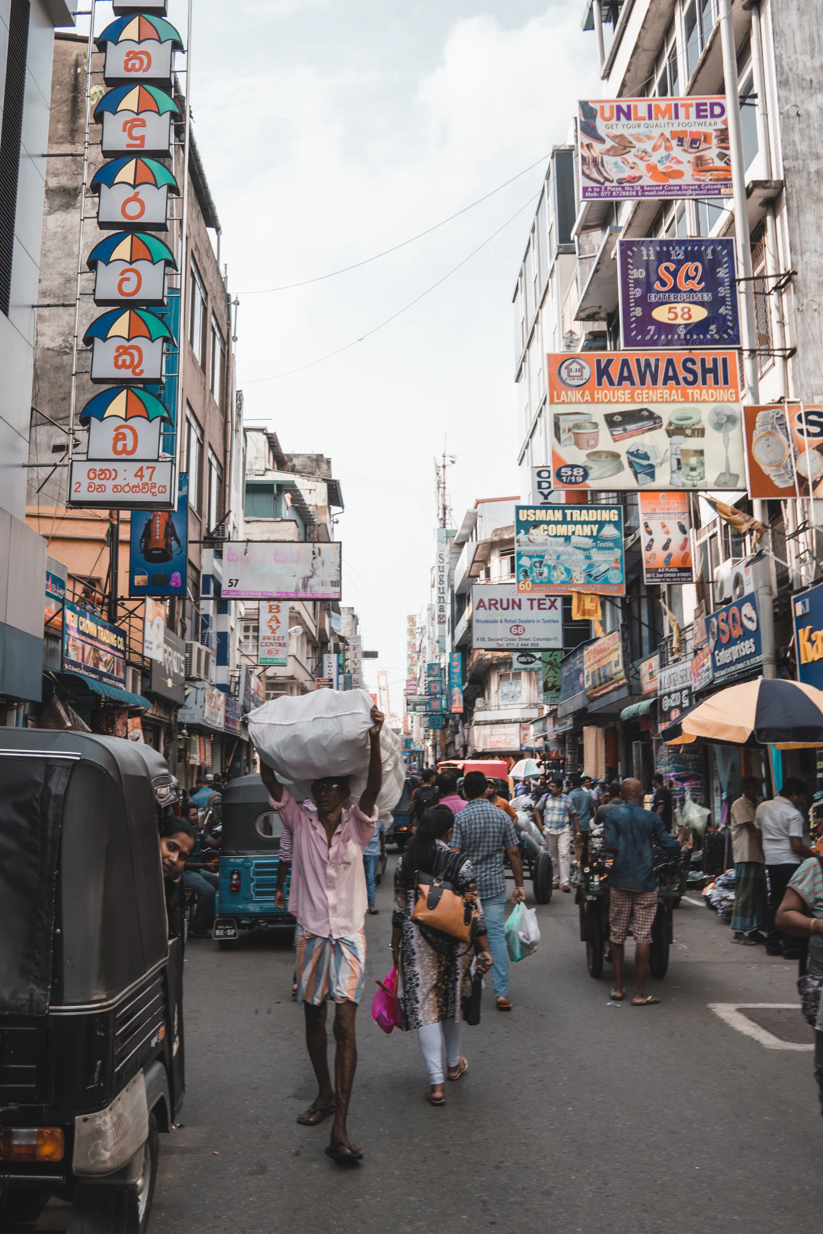 Travel photograph: People, signs, awnings and vehicles fill a busy Colombo market street.