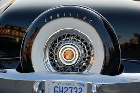 A close-up of the back of a vintage car showcasing a Cadillac emblem on a spare tire cover with intricate chrome detailing. The Ontario license plate is visible at the bottom.