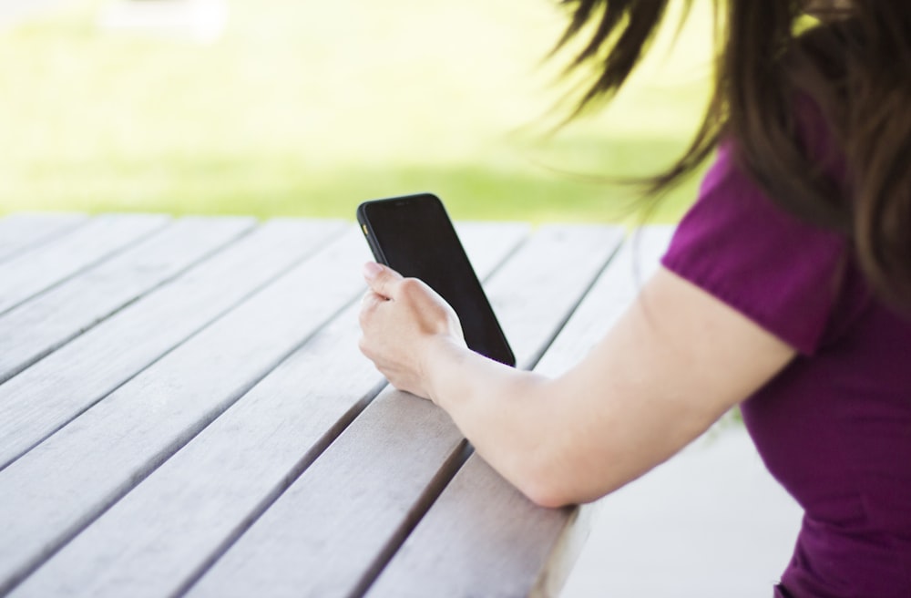 woman sitting beside table holding smartphone