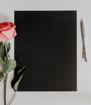 orange rose flower beside notebook and pen