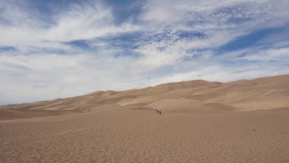 a couple of people walking across a sandy field