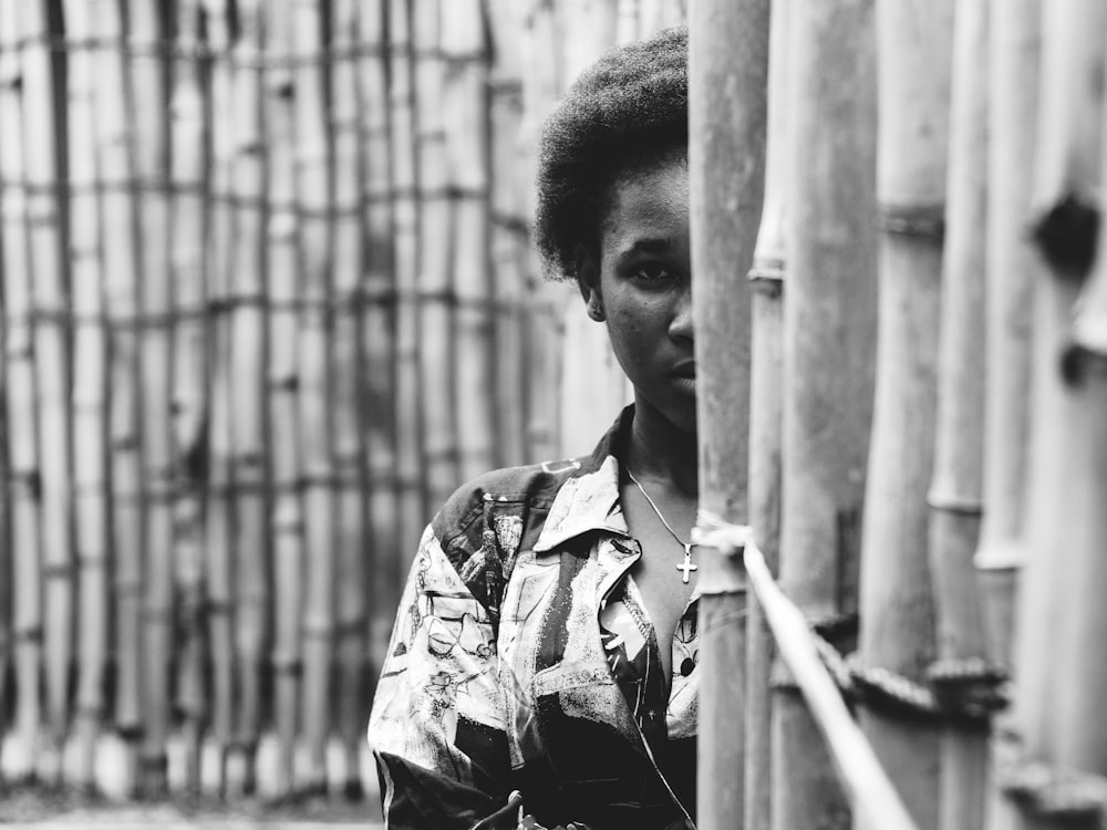 grayscale photo of person hiding on bamboo wall