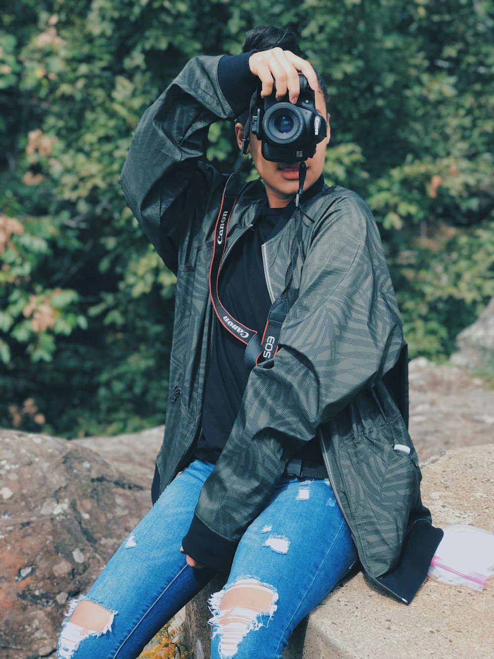 man holding camera while sitting on rock formation