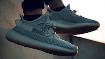 A pair of stylish sneakers with a textured design, laces, and rubber soles, shown in an outdoor setting with soft lighting.