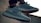 A pair of stylish sneakers with a textured design, laces, and rubber soles, shown in an outdoor setting with soft lighting.