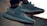 A pair of stylish sneakers with a textured design, laces, and rubber soles, shown in an outdoor setting with soft lighting.