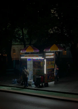 A colorful food cart serving international dishes with happy customers enjoying their meals under a bright market tent.