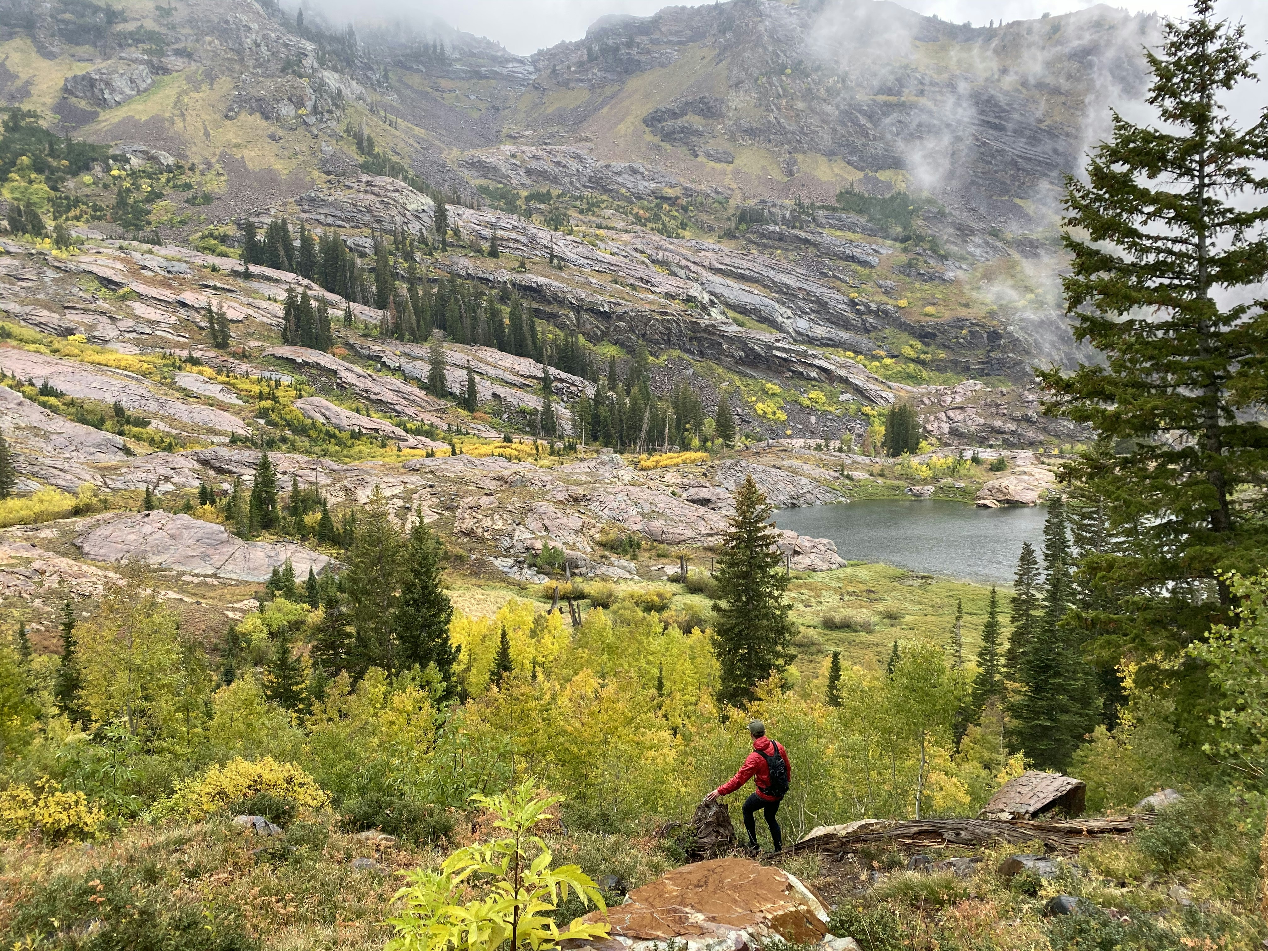 Photographie aérienne d’un homme debout sur une colline rocheuse regardant la montagne et le plan d’eau pendant la journée