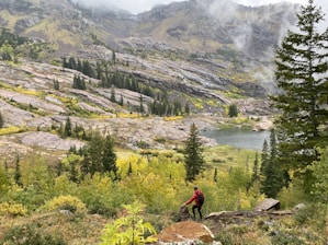 aerial photography of man standing on rocky hill viewing mountain and body of water during daytime