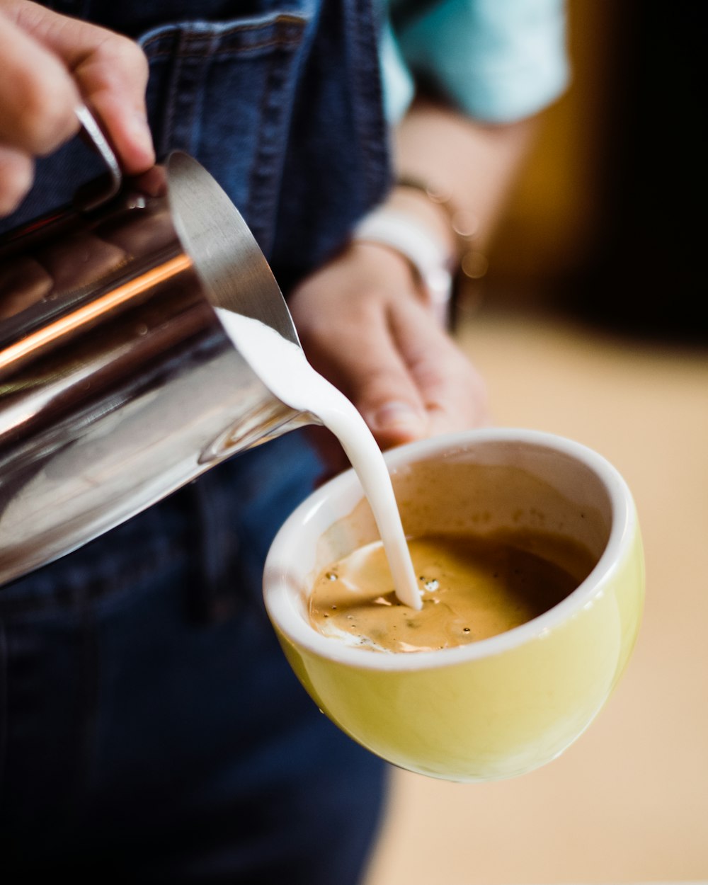 person pouring milk on coffee cup