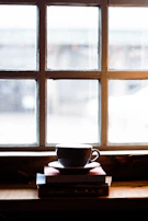 A peaceful corner with journals stacked beside a cup of tea and soft natural light.