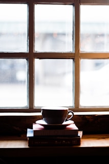 A cozy nook with a stack of well-loved books, a steaming cup of tea, and soft natural light filtering through a window.