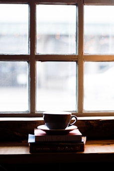 A cozy nook with a stack of well-loved books, a steaming cup of tea, and soft natural light filtering through a window.