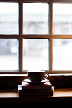 A softly lit corner featuring a stack of well-loved books, a brass candle holder, and a cup of espresso on a linen cloth.