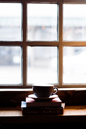 Softly lit cozy nook with warm beige tones, a stack of books, and a steaming cup of tea by a window.