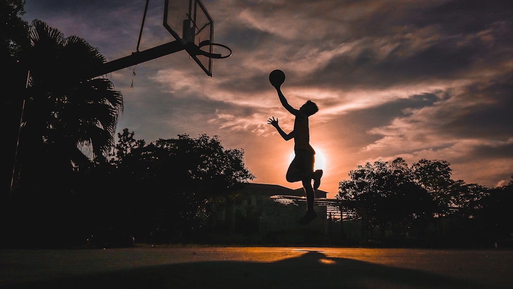 silhouette of boy jumping shooting ball