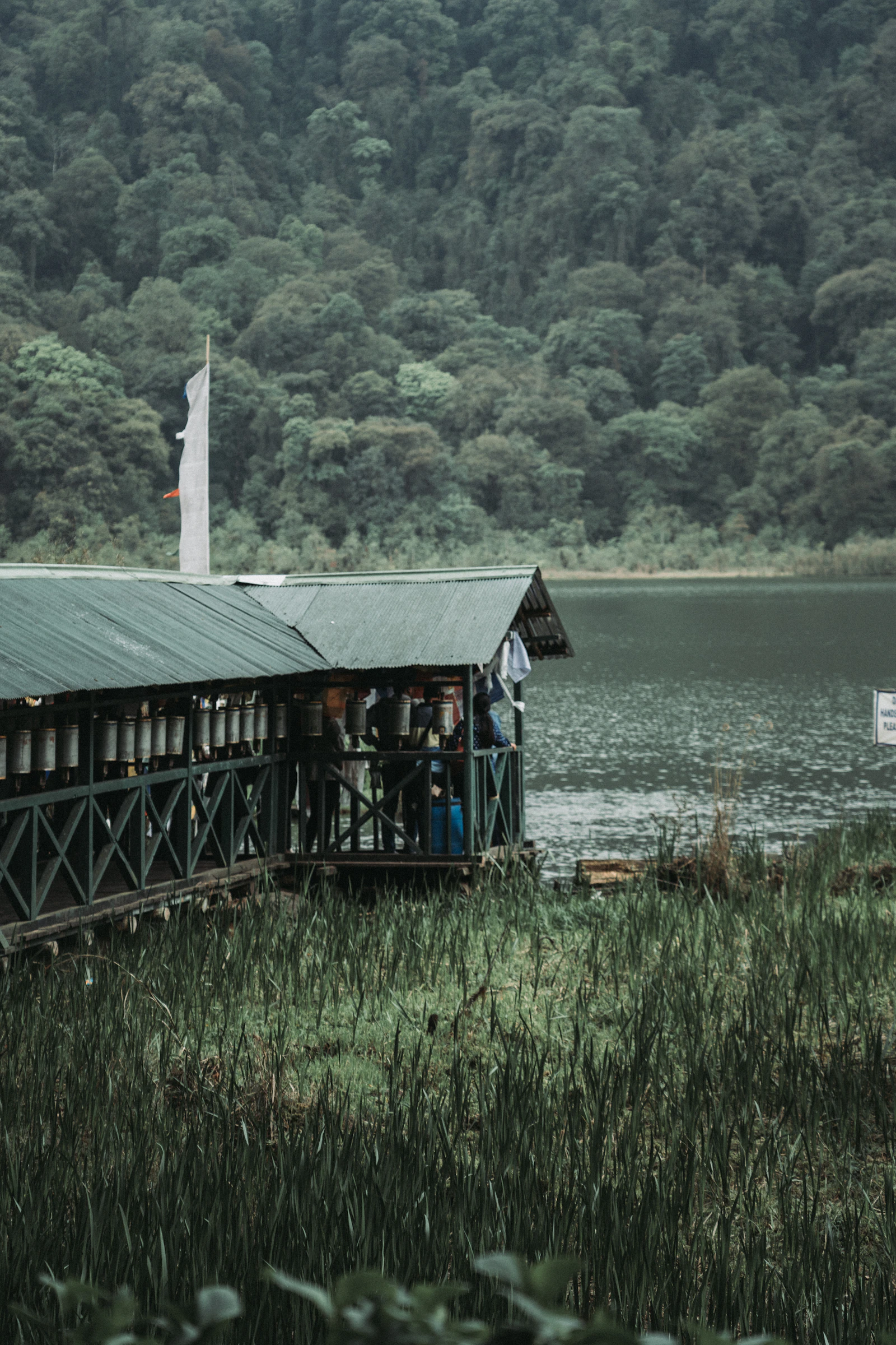 A covered wooden jetty lined with prayer wheels running out onto a forest lake in Sikkim