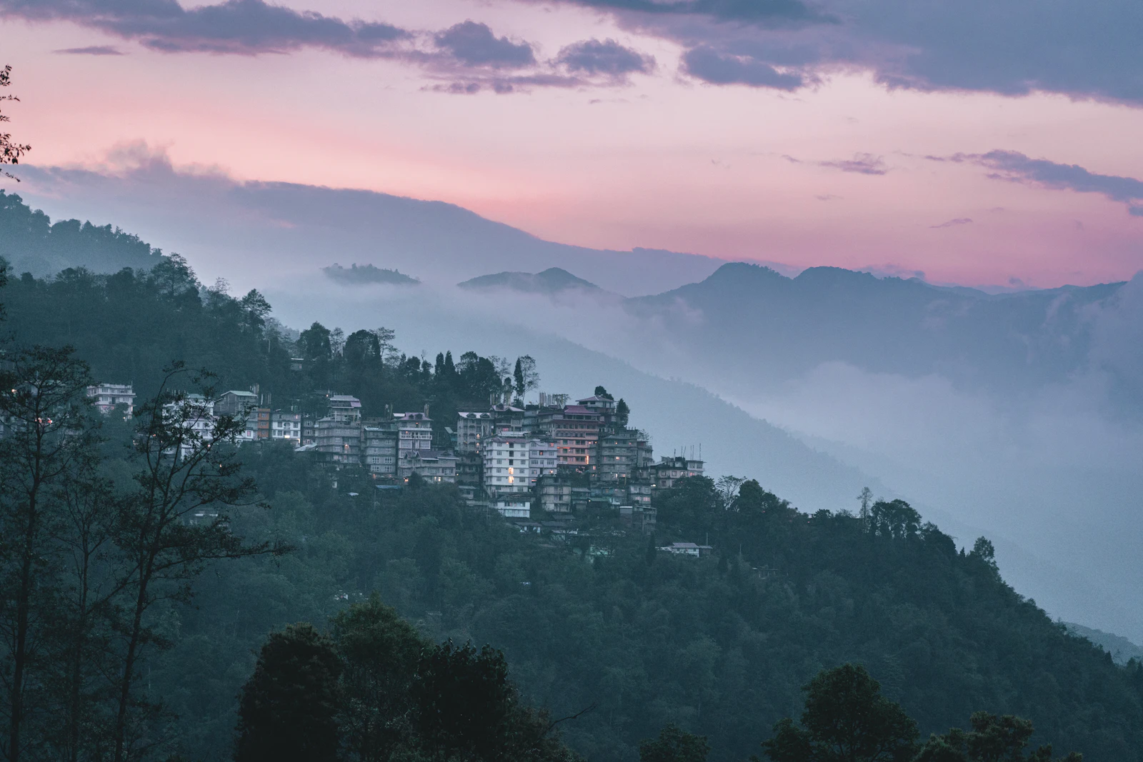 Pelling's houses along their forested ridge at dusk, cloud filling the valleys below a pink sky