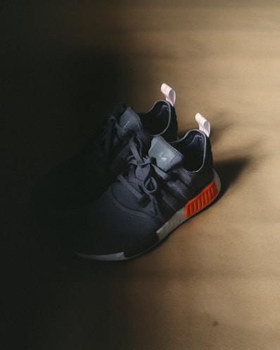 A pair of black and orange running shoes placed on a dark surface with subtle shadows.