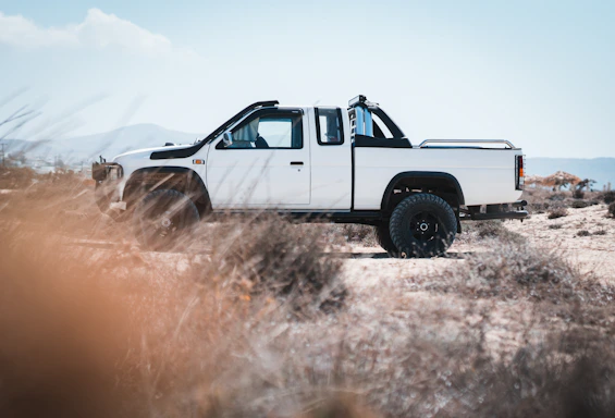 A rugged pickup truck parked on a dusty oil field road at sunset in Vaca Muerta.