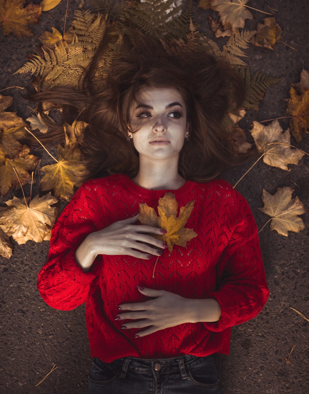 빨간 스웨터를 입은 여자가 마른 나뭇잎 옆에 누워 있다