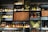 A wall of shelves filled with various bottles of liquor, including whiskey, gin, and other spirits. The shelves are arranged in a grid pattern and feature textured glass and decorative panels with earthy and abstract designs. Soft lighting highlights the bottles, creating an inviting and sophisticated atmosphere.