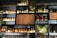 A wall of shelves filled with various bottles of liquor, including whiskey, gin, and other spirits. The shelves are arranged in a grid pattern and feature textured glass and decorative panels with earthy and abstract designs. Soft lighting highlights the bottles, creating an inviting and sophisticated atmosphere.