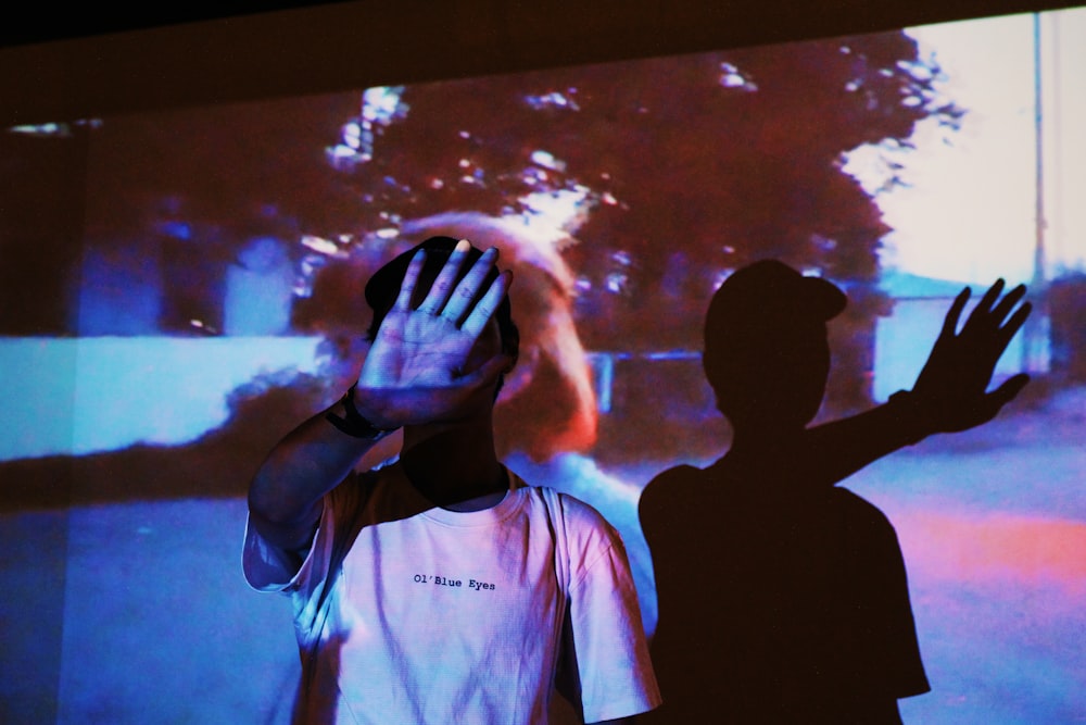 man wearing white and black crew-neck t-shirt standing while covering face using right palm