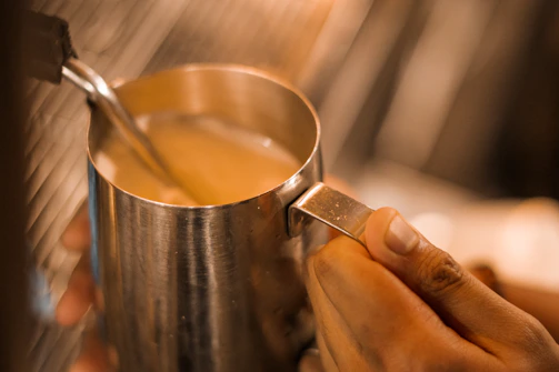 Detailed shot of a steaming pitcher creating perfect milk foam texture.