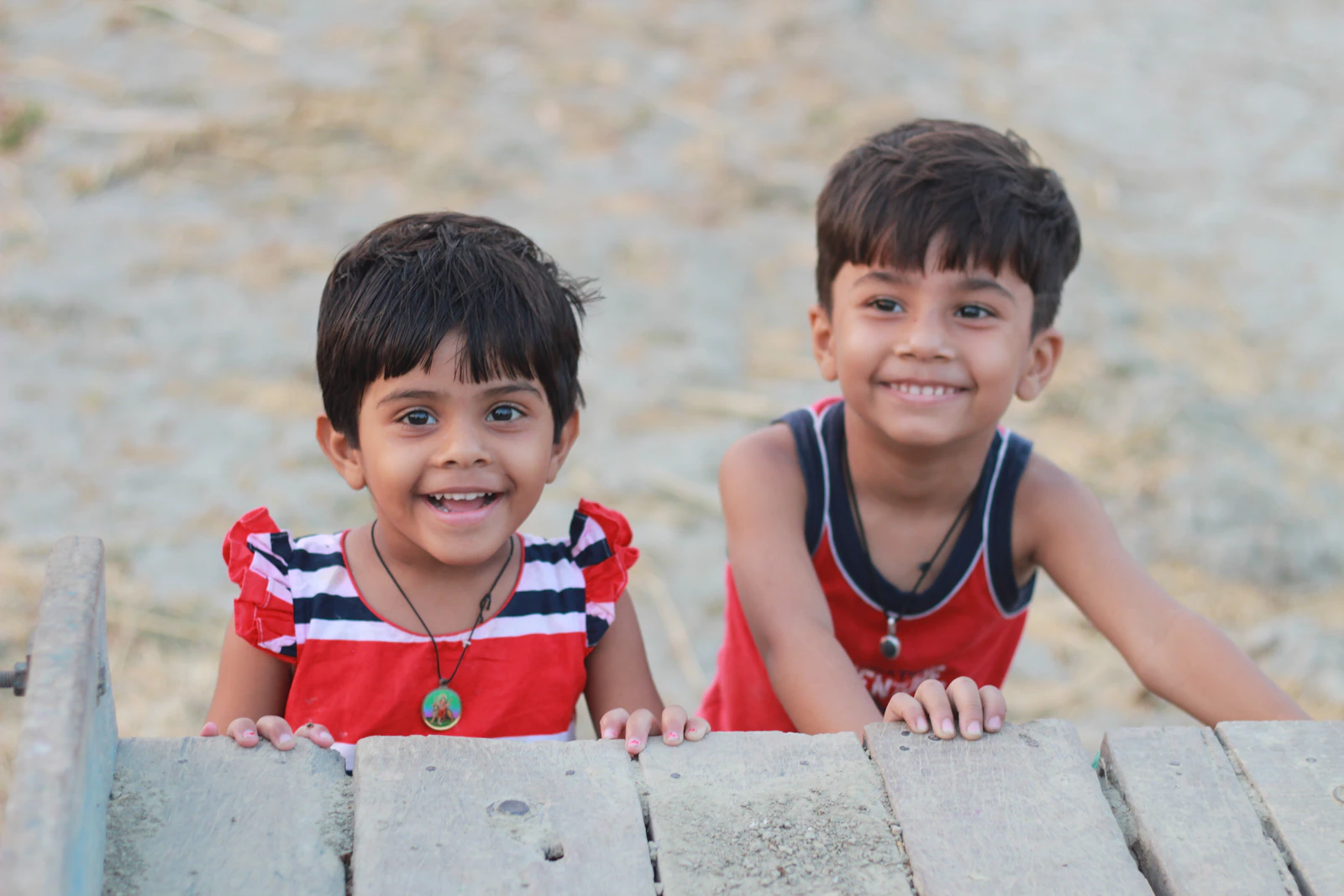 A girl and a boy smiling over a wooden rail.