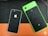 Two smartphones are placed on a textured surface. One phone has a green frame with a black honeycomb-patterned back and a fingerprint sensor. The other phone has a black and white color scheme with a similar honeycomb pattern and a prominent logo.